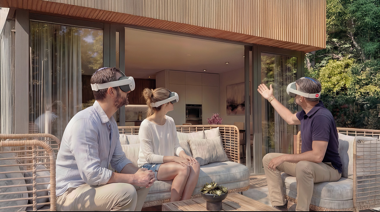 Drie personen met VR-brillen zitten op een bank bij een moderne woning, met grote ramen en een groene omgeving.