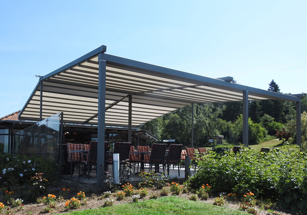 Überdachung mit Markisentuch und Sitzmöglichkeiten, umgeben von einer grünen Terrassensituation.