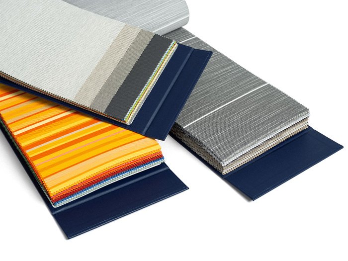 Stofstalen in verschillende kleuren en patronen, waaronder grijs, geel en oranje. Stofstalen in verschillende kleuren en patronen, waaronder grijs, geel en oranje.