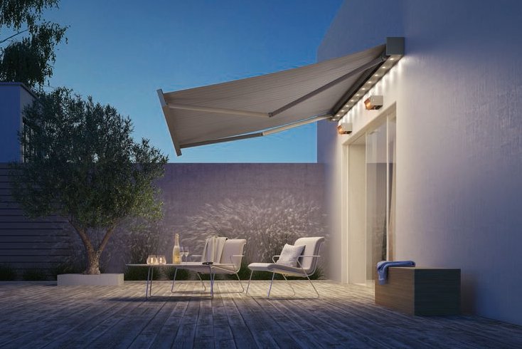 Een moderne terrassituatie met een uitgevouwen zonnescherm en zachte verlichting, onder een heldere blauwe lucht.