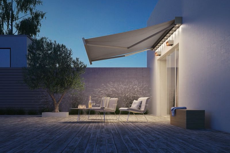 Een moderne terrassituatie met een uitgevouwen zonnescherm en zachte verlichting, onder een heldere blauwe lucht.