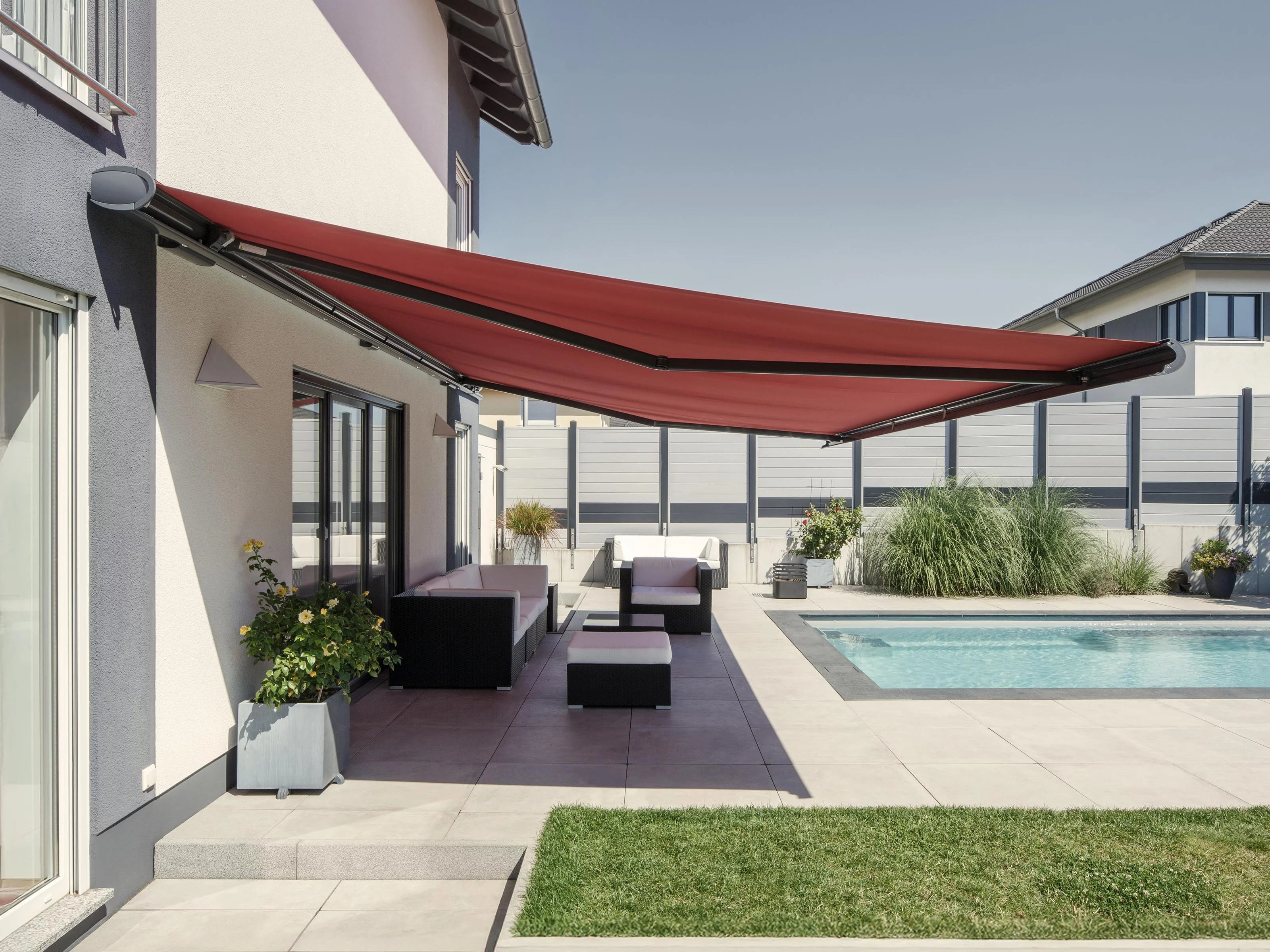 Terrassensituatie met een rode markise, zwembad en moderne woning op een zonnige dag.