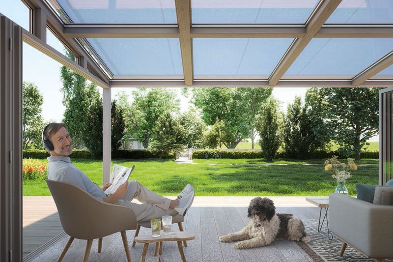 Een moderne terrasoverkapping met een lichtblauwe kleur en een houten constructie, ingericht met meubels en een hond.