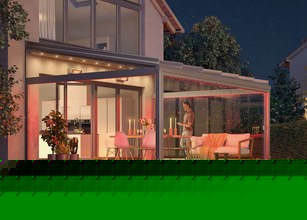 Een moderne overkapping met glazen wanden, verlicht door warme kleuren, in een terrassensituatie bij nacht. 