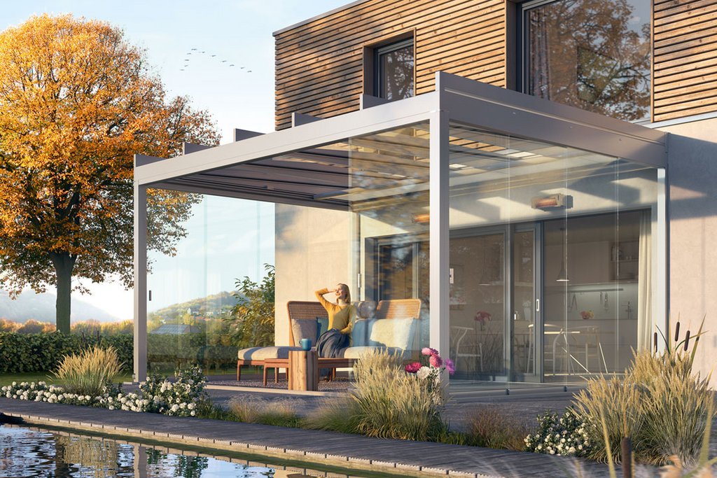 Moderne overkapping met glazen wanden en een terras in een tuin met waterpartij en bomen.