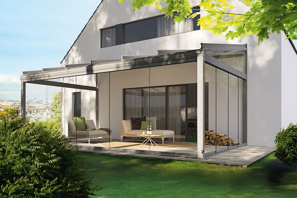 Moderne woning met glazen schuifwanden en een overkapping, omringd door groen en een terras.