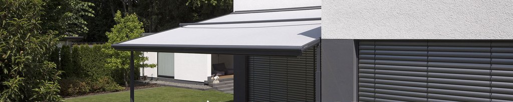 zonnescherm in lichte kleur, bevestigd aan een moderne gevel, met een groene omgeving en een strakke vorm.