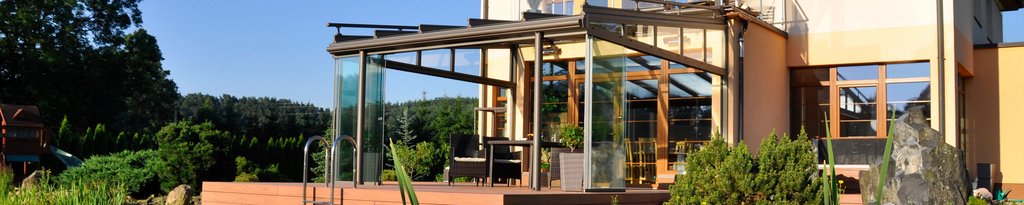 Moderne woning met glazen elementen en een overkapping, omgeven door groene planten en een terras.