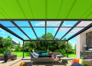 Terrassensituatie met een overkapping, groene zonnescherm en een ontspannende persoon op een bank. 