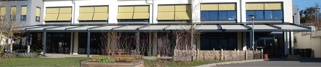 Moderne gebouw met gele luifels en overkapping. Groen gras en houten hekwerk zichtbaar. Moderne gebouw met gele luifels en overkapping. Groen gras en houten hekwerk zichtbaar.