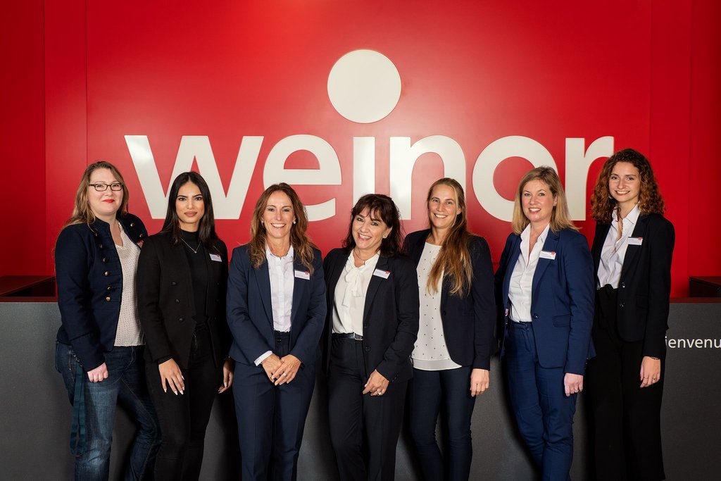 Groep vrouwen in zakelijke kleding voor een rode achtergrond met een merknaam. Groep vrouwen in zakelijke kleding voor een rode achtergrond met een merknaam.