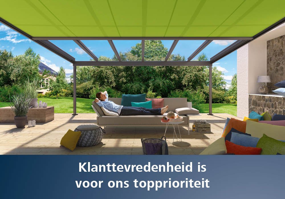 Een man ligt op een ligstoel onder een groene zonnescherm met een terras en groen gras op de achtergrond.